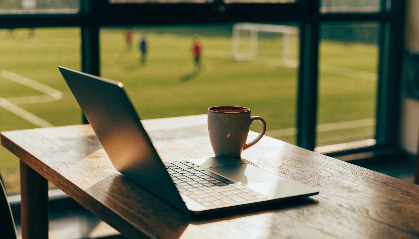 Clubhouse table with laptop and tea, football pitch through the window
